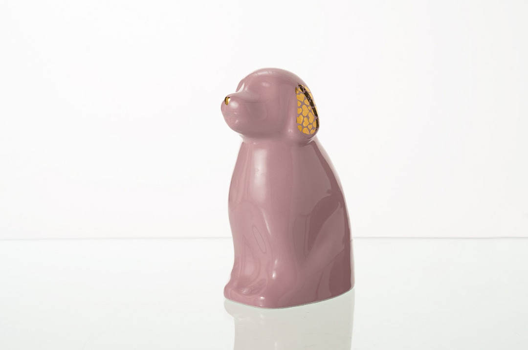 Soft pink dog ceramic urn with gold lattice ear detail on a reflective surface
