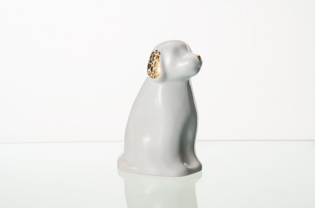 Side view of a pale ceramic dog urn showing a curved body and gold lattice ears on a white backdrop.
