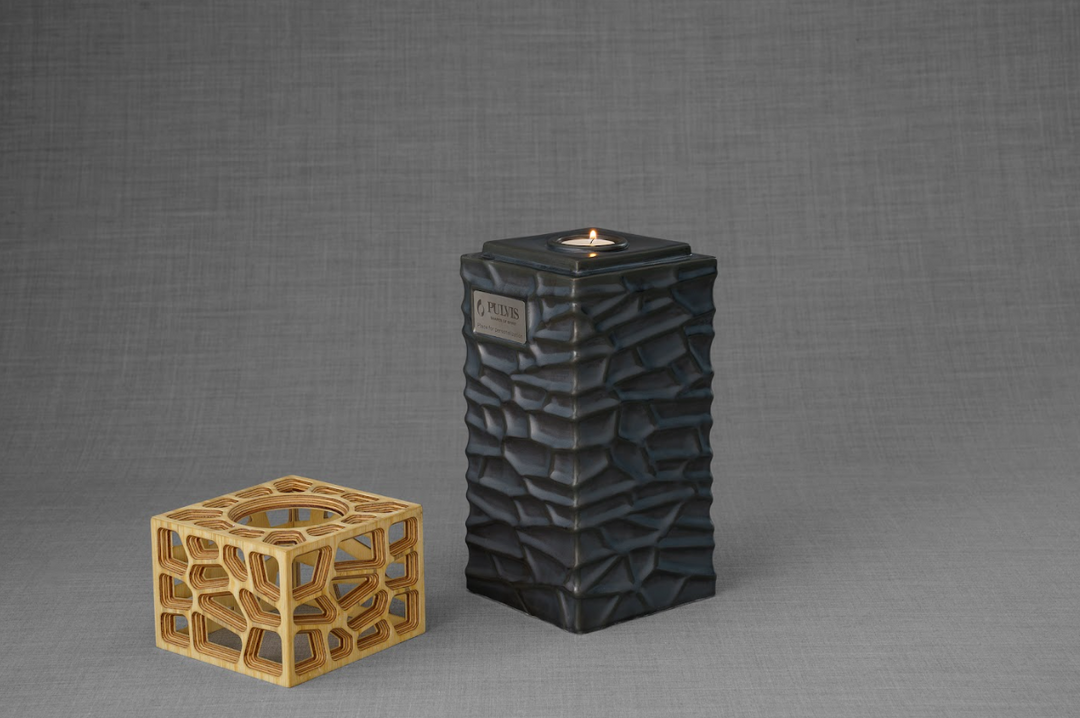 Everlasting Flame urn in dark textured ceramic with a lit tealight on top beside a wooden lattice cube