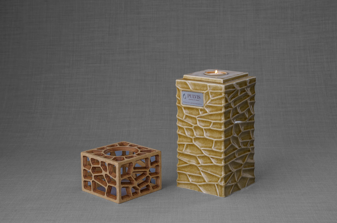 Tall stone pattern ceramic urn with a lit candle on top beside a geometric wooden lattice candle holder.