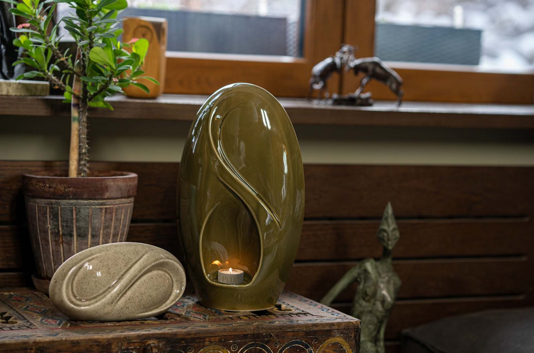 Eternity Ceramic Urn in olive green with a curved open notch and a lit candle inside.