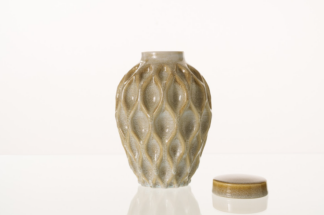 Cream speckled ceramic urn with a flowing lattice pattern and a separate lid beside it.