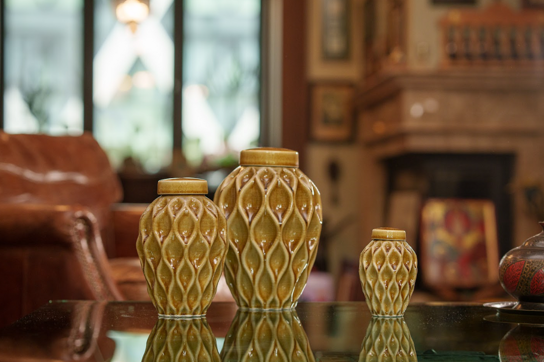 Set of three Echo ceramic urns in varying sizes with the same lattice design displayed on a glass table in a warm living room.