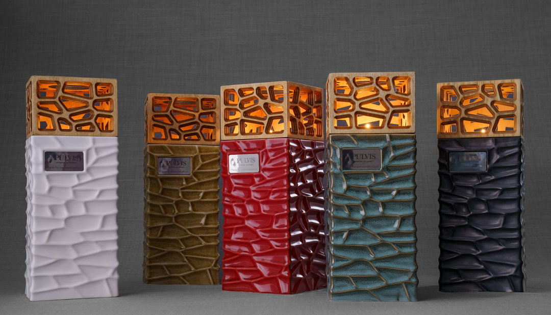 Five tall ceramic urns with orange lattice caps and textured stone bodies in white, tan, red, teal, and black