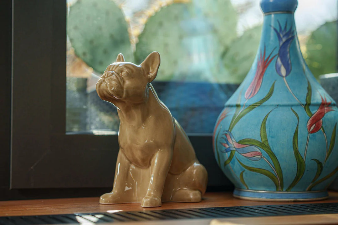 Brown glazed French Bulldog ceramic urn bottom filled displayed on a wooden shelf beside a blue floral vase