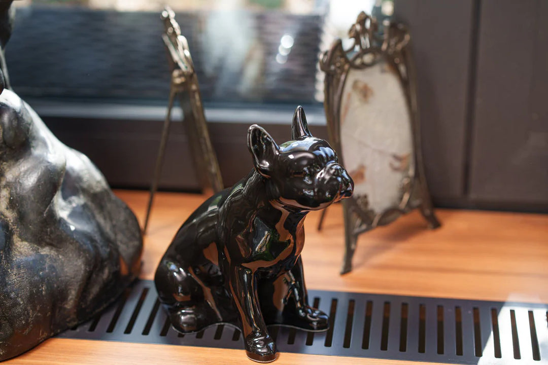 Glossy black French Bulldog ceramic urn on a wooden surface with decorative items in the background
