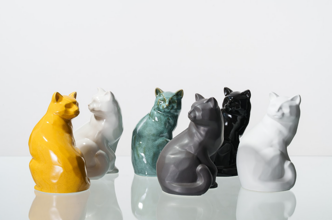 Row of colorful ceramic cat figurines in yellow white teal gray and black on a reflective surface.