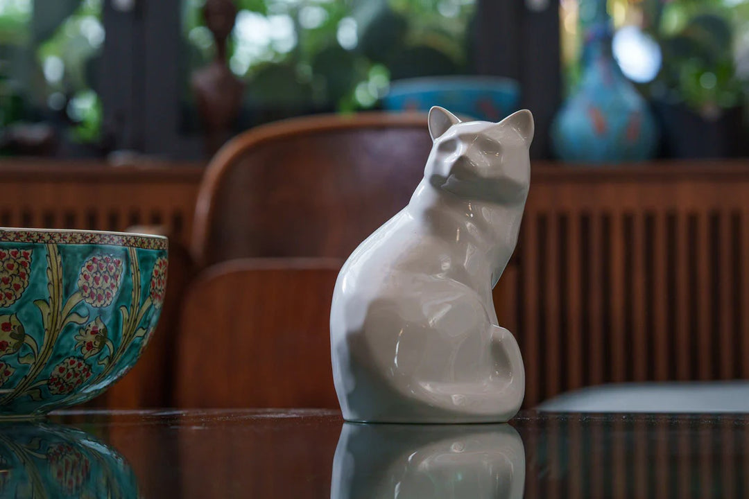 Felix cat urn in white glossy ceramic on a reflective table in a cozy room.