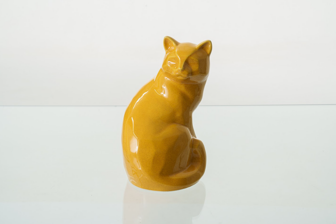 Orange Felix cat ceramic urn with a glossy glaze resting on a reflective surface