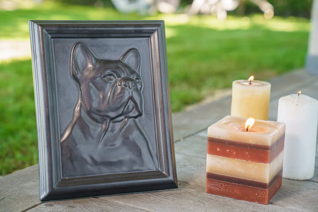 Dark framed French bulldog relief with three candles on a wooden surface outdoors