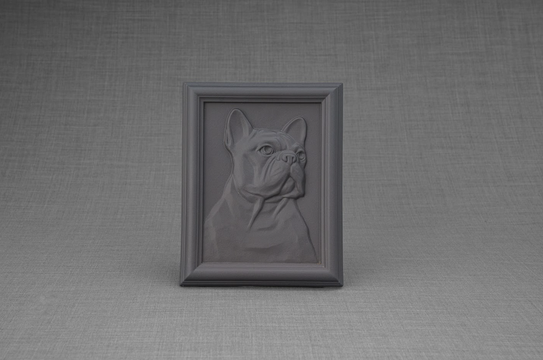 Close up of a dark framed dog relief portrait on a pedestal in a garden setting.