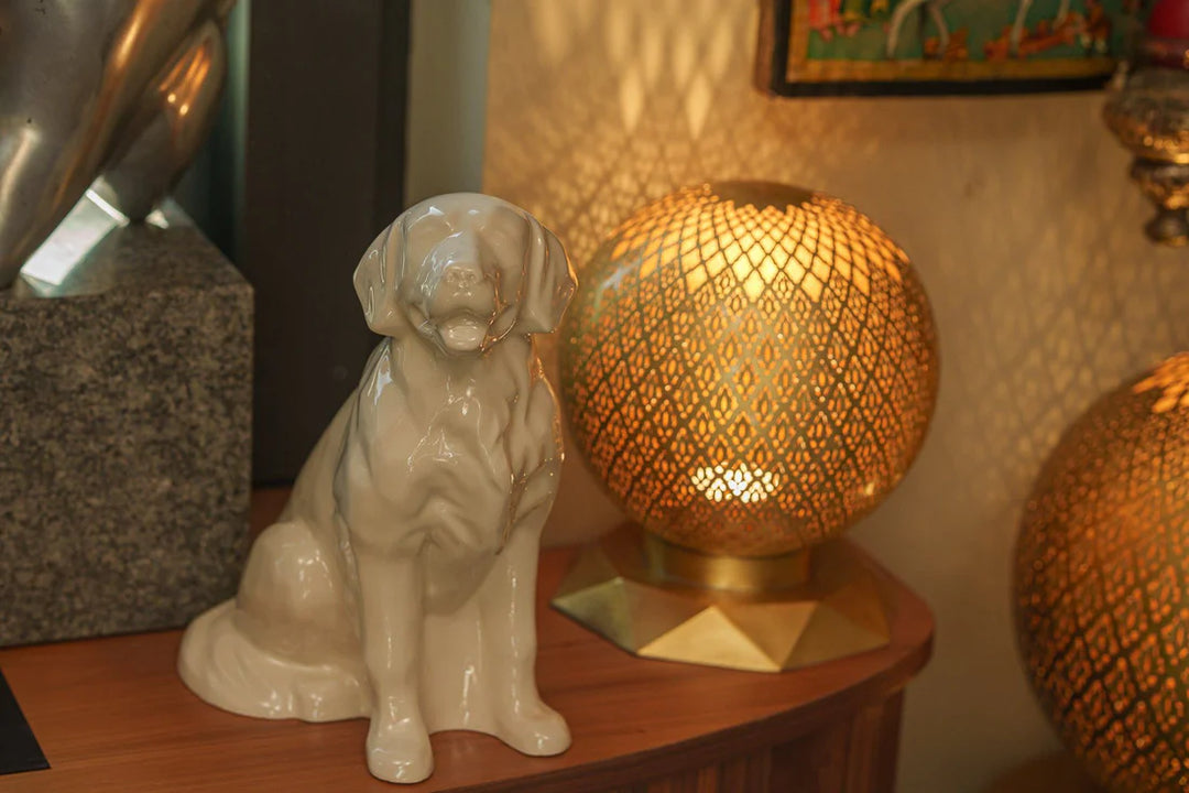 Beige ceramic Golden Retriever urn on a wooden surface with decorative lamps in the background