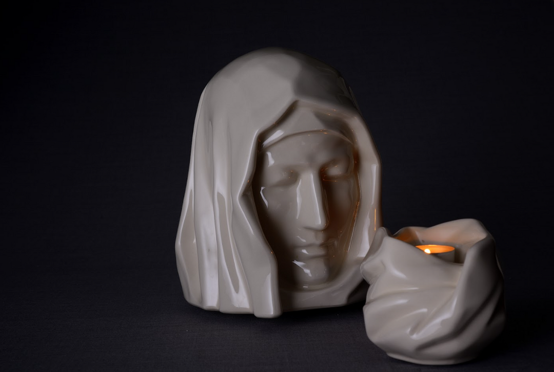 White Holy Mother urn with a lit candle in a small holder beside the draped veil.
