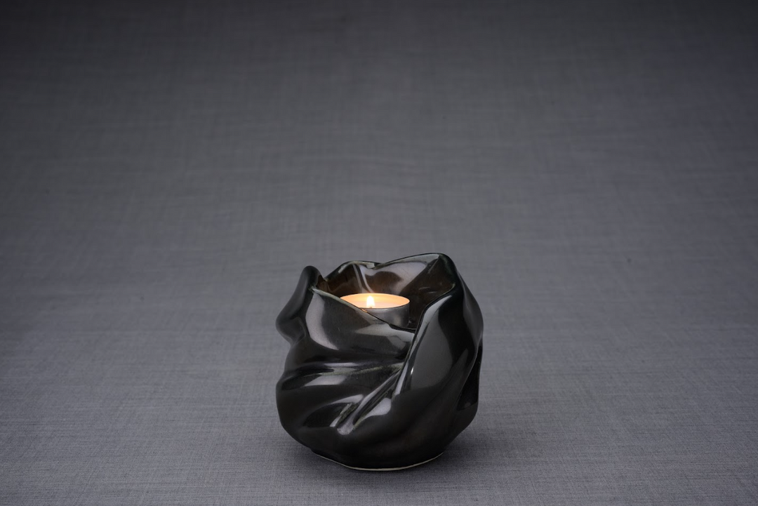 The Holy Mother black ceramic urn with sculpted draped folds and a lit tealight at the opening.