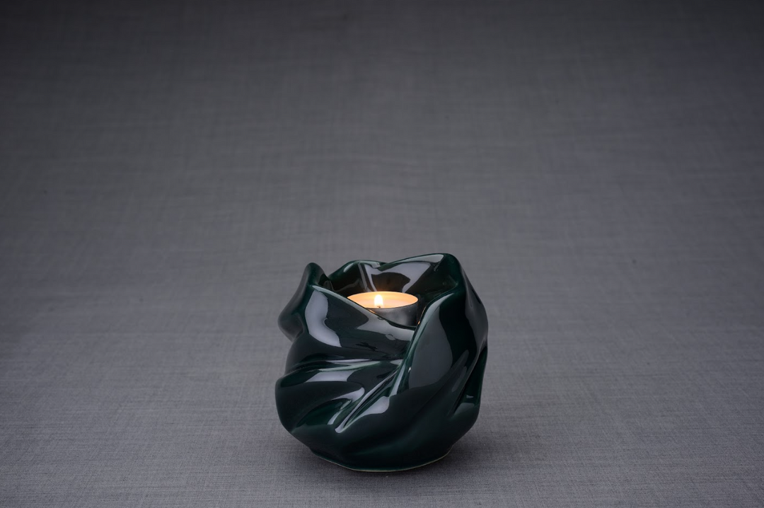 Dark green glazed ceramic Holy Mother urn with a lit candle inside on a gray backdrop