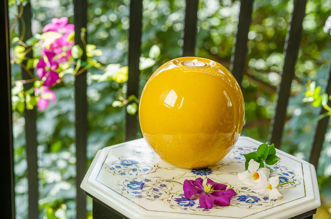 Harmony ceramic urn in warm yellow glaze with built in candle holder on top on an outdoor table.