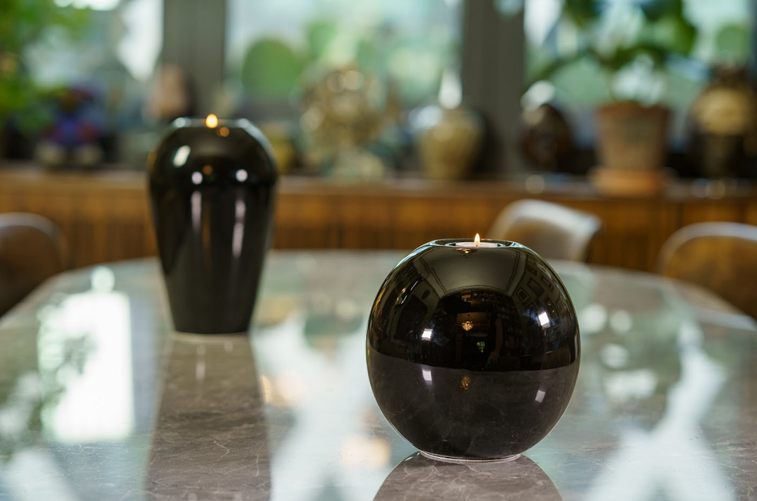 Glossy black Harmony ceramic urn with a candle holder on a marble table, blurred background vase.