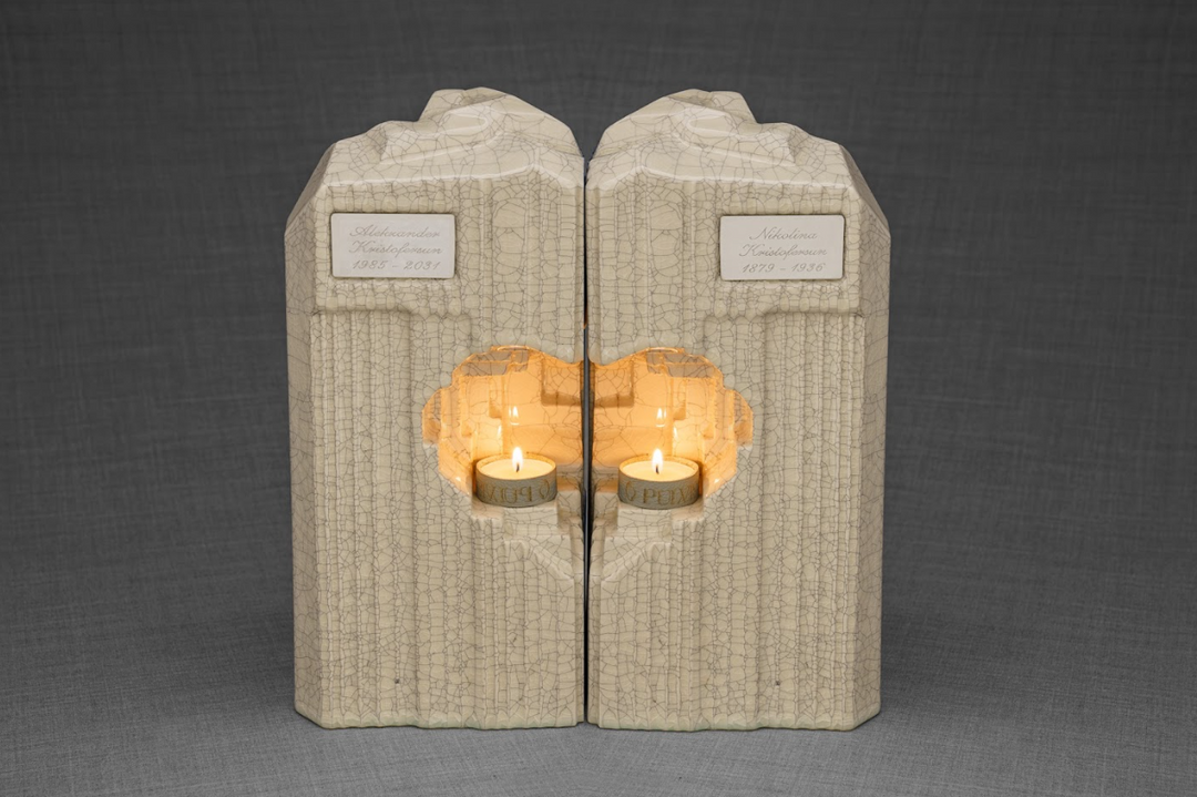 Beige crackled ceramic companion urns standing side by side with twin heart candle niches and lit flames.