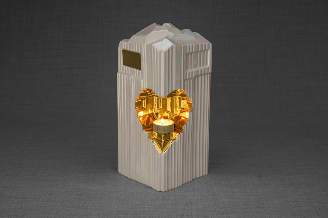 Pale ribbed Heart ceramic urn with a gold heart insert and a lit candle in the heart window.