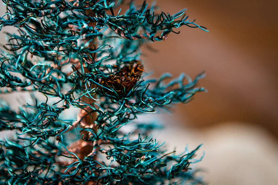 Close up of teal Spruce Tree of Life branches showing intricate wire tips against a soft blurred background.