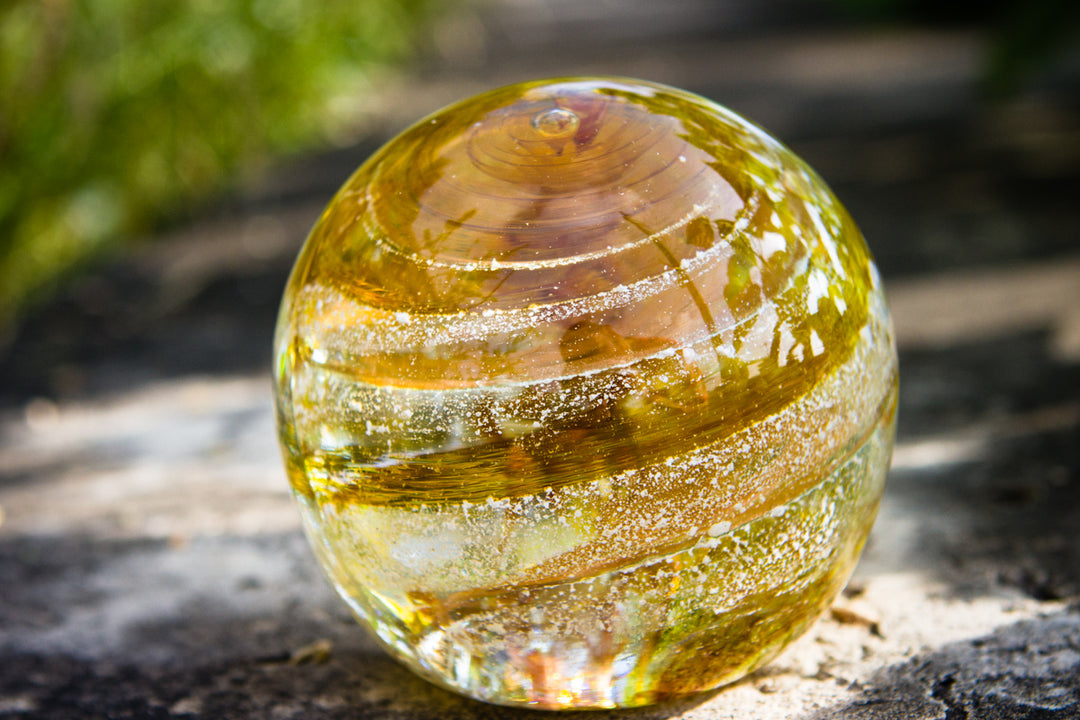 Amber Sparkle Orb with gold swirls and white speckles outdoors on a rock