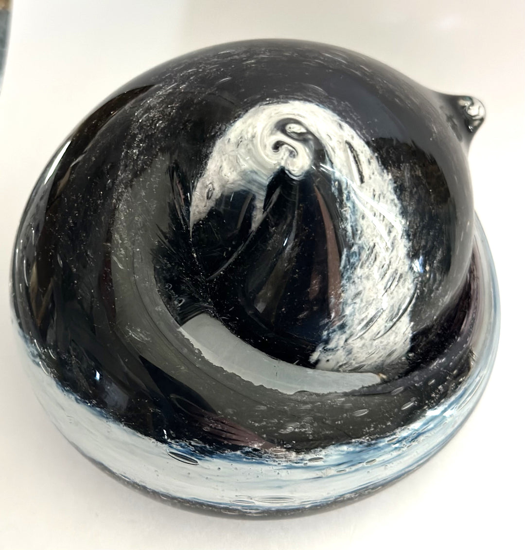 Smoky swirled glass cat paperweight resting on a wooden surface.