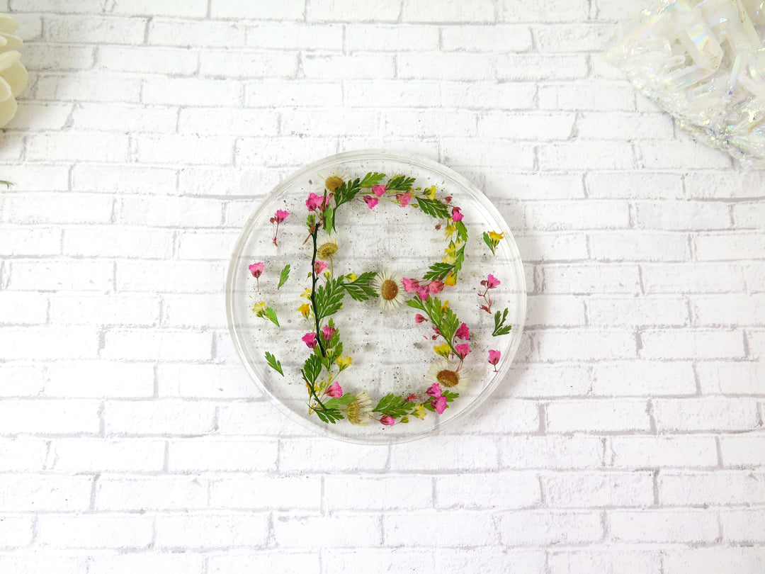 Round memorial coaster with pink and yellow flowers arranged around the edge on a white surface.