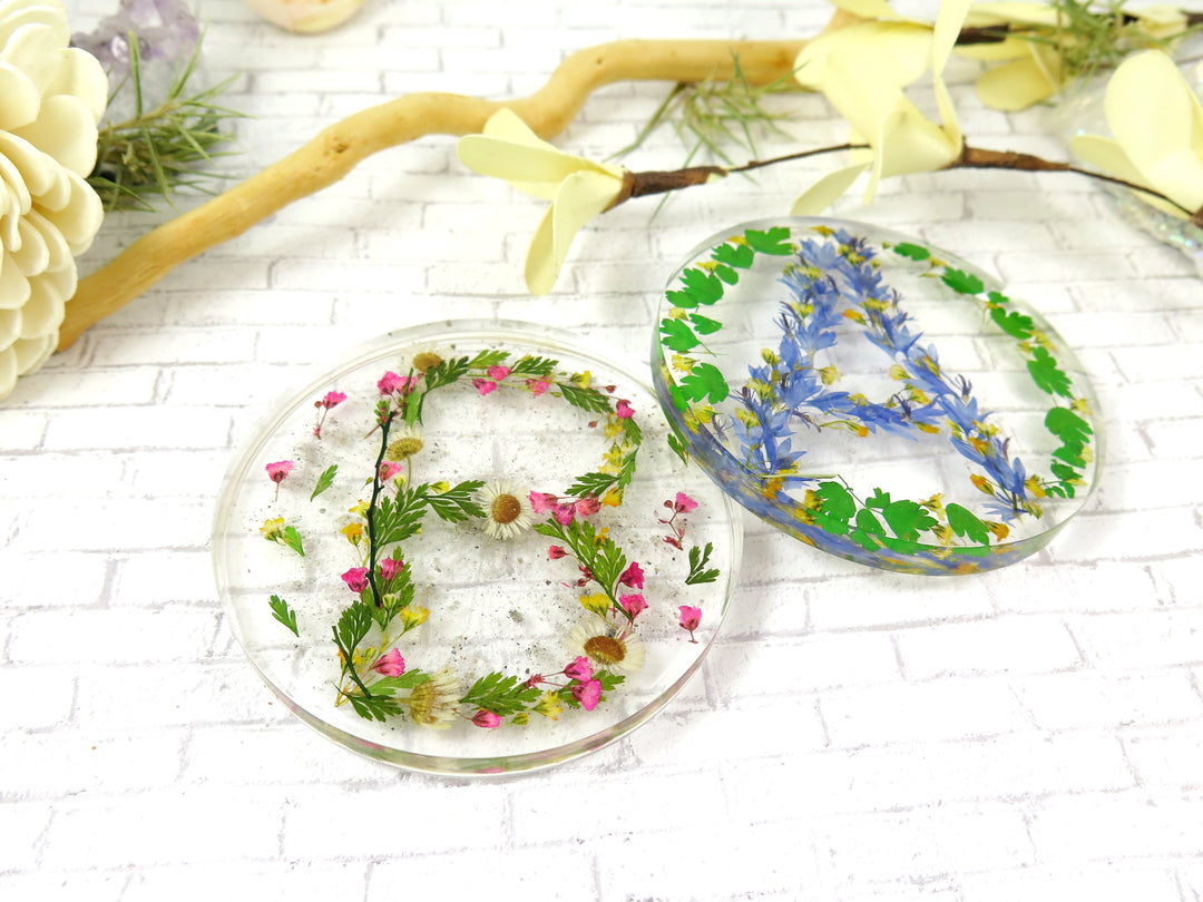 Round resin coaster embedded with cremation ash and pressed flowers forming a floral letter.