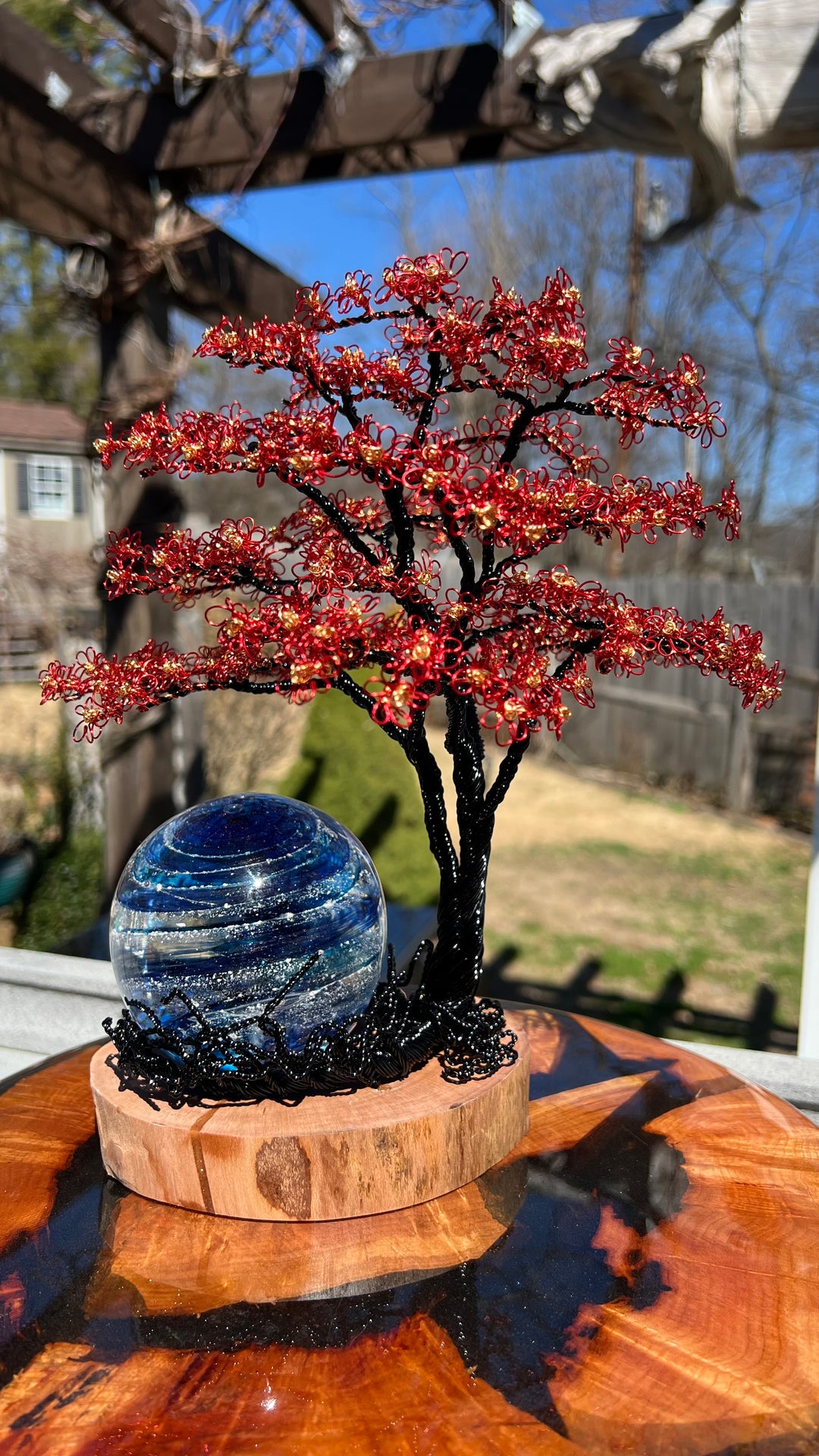 Flamboyant Tree of Life wire sculpture with red and gold blossoms beside a blue Sparkle Orb on a round wooden base