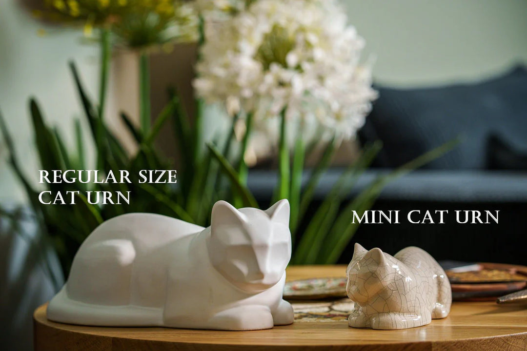 Regular size cat urn and mini cat urn displayed on a wooden table with greenery in the background
