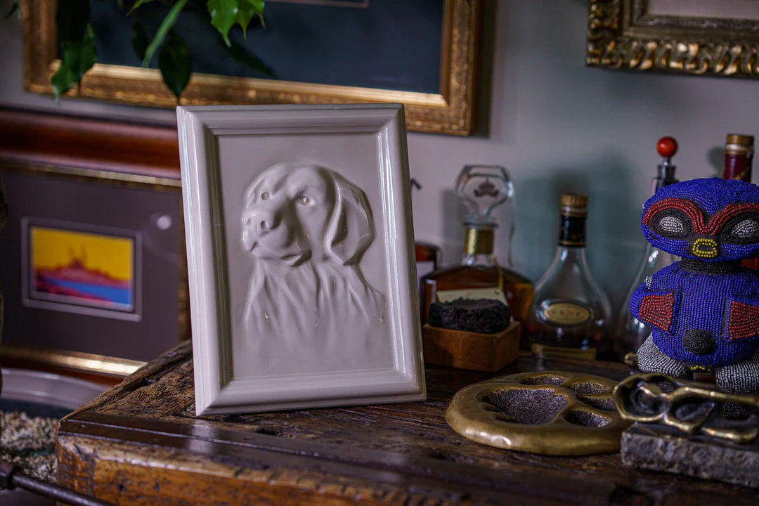 White framed ceramic relief of a Labrador retriever on a wooden surface.