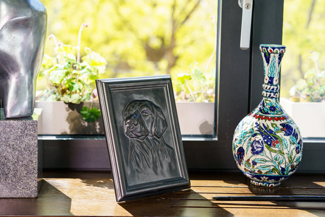 Labrador portrait frame leaning on a wooden windowsill beside a colorful ceramic vase.
