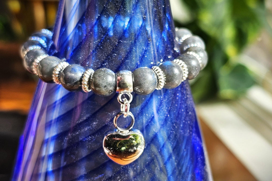 Labradorite bead bracelet with a silver urn heart charm wrapped around a cobalt blue glass bottle.