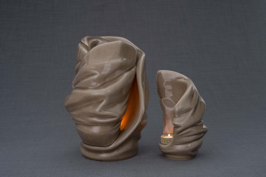 Two Light Ceramic Urns with draped fabric textures in taupe, one large and one small, each with a warm glow.