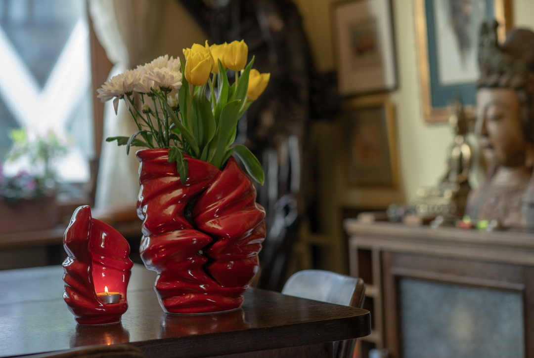 Red Light Ceramic Urn used as a vase with yellow tulips and white flowers on a wooden table, with a small candle urn beside