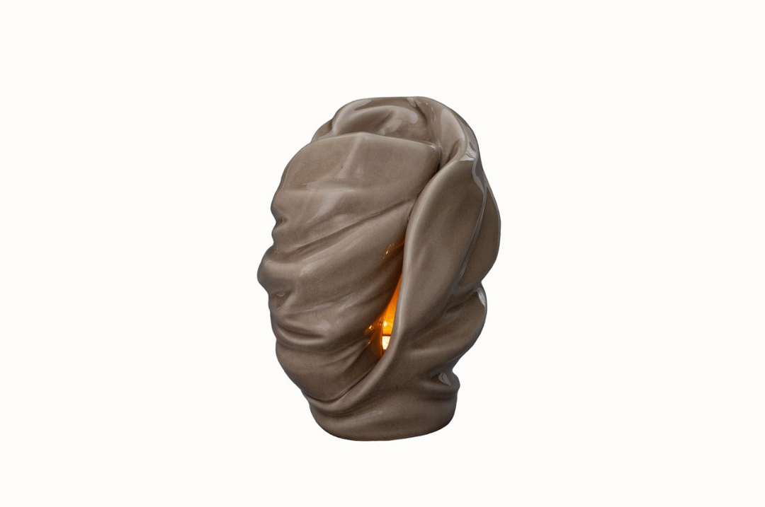 Light Ceramic Urn with sculpted draped folds and a warm candle glow visible through the opening.