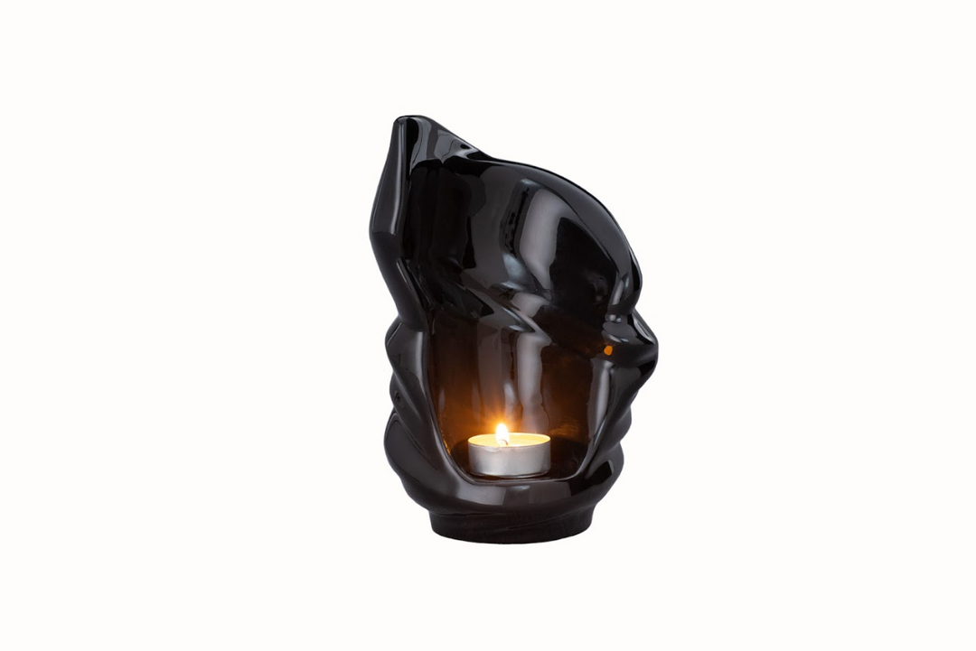 Shiny black Light Ceramic Urn featuring a twisting sculptural exterior and a glowing candle inside.