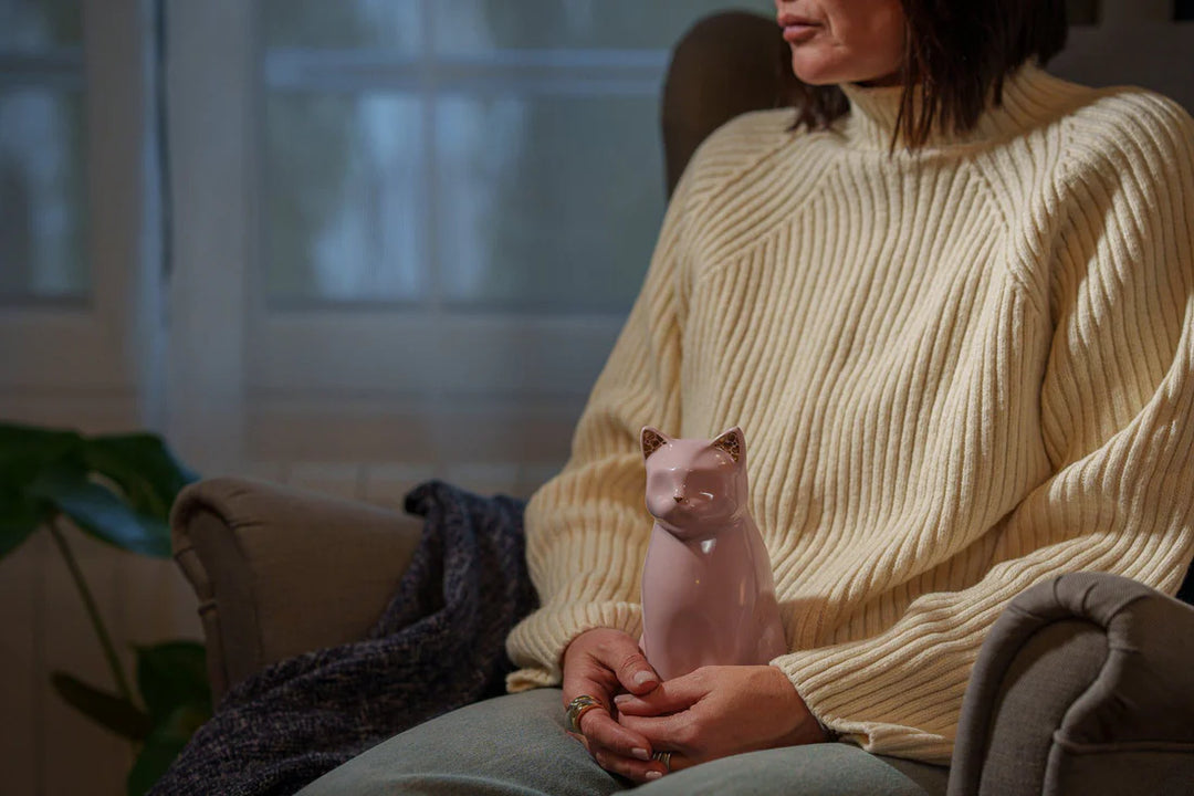 Person in cream sweater holding a pink Meow cat ceramic urn with a glossy finish.