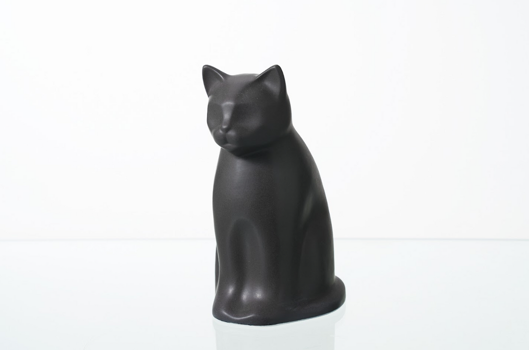 Seated matte black Meow cat ceramic urn against a plain white backdrop.
