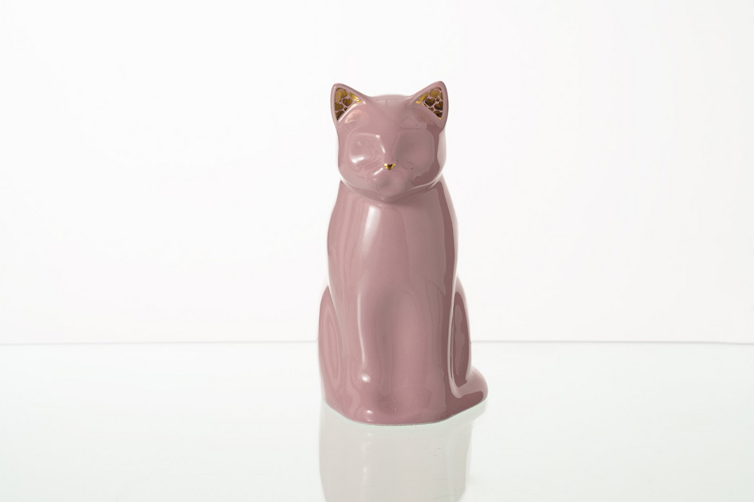 Pastel pink Meow cat ceramic urn with gold ear accents on a reflective surface