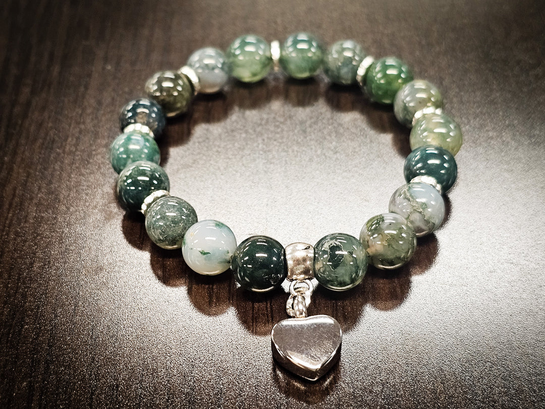 Moss agate bead bracelet with an urn heart charm on a dark surface.