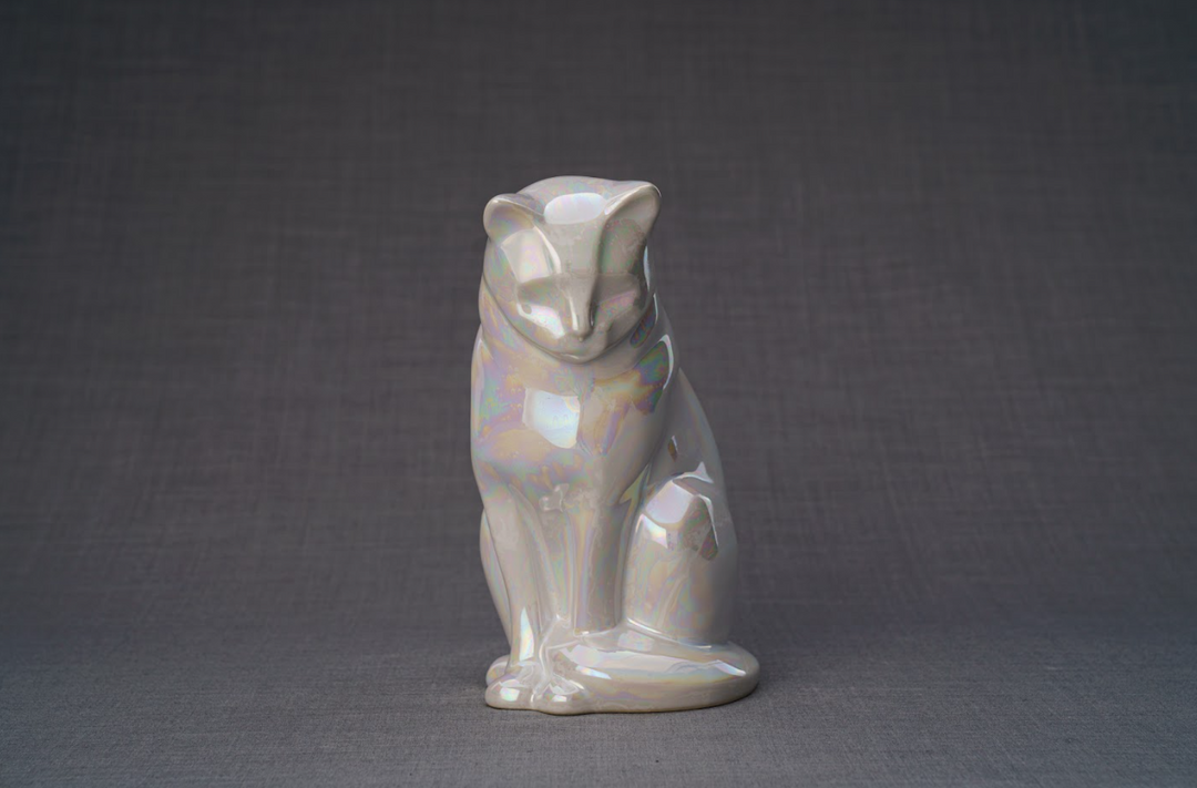 Iridescent pearl white ceramic cat urn in a seated pose with a reflective glaze