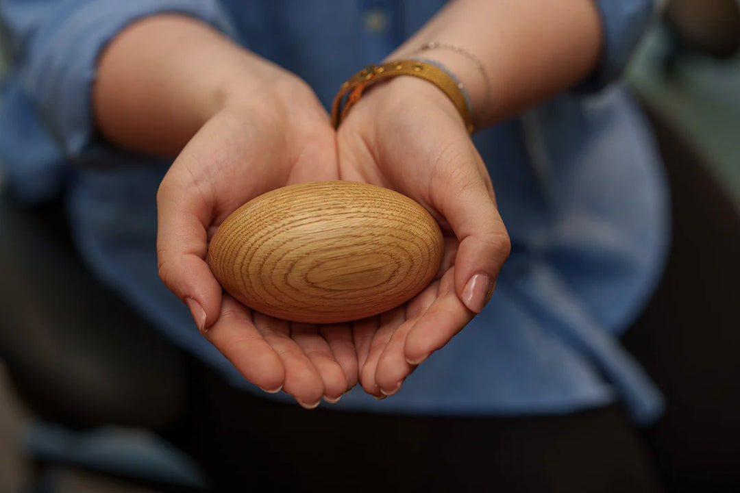 Hands cradle a smooth oval wooden keepsake urn with a warm natural finish
