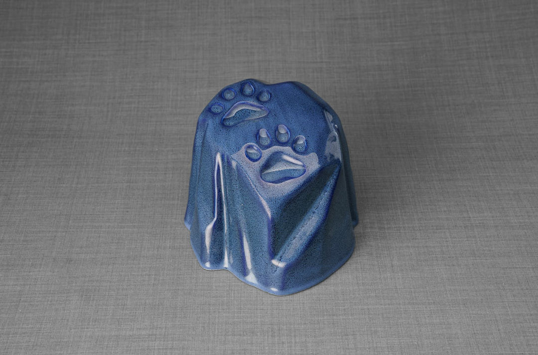 Blue paw print ceramic urn shaped like a natural stone with paw imprints for a pet memorial.