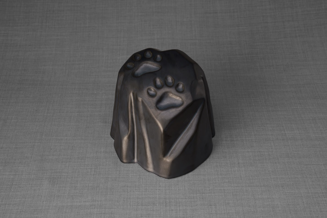 Dark bronze paw print ceramic urn with a faceted stonelike form for a pet memorial.