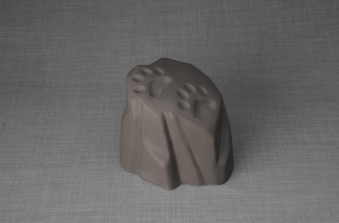 Stone shaped paw print ceramic urn with subtle paw impressions on top resting on a gray surface