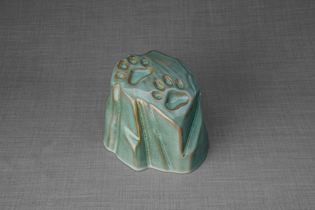 Teal glazed paw print ceramic urn shaped like a natural stone with paw impressions for home or garden.
