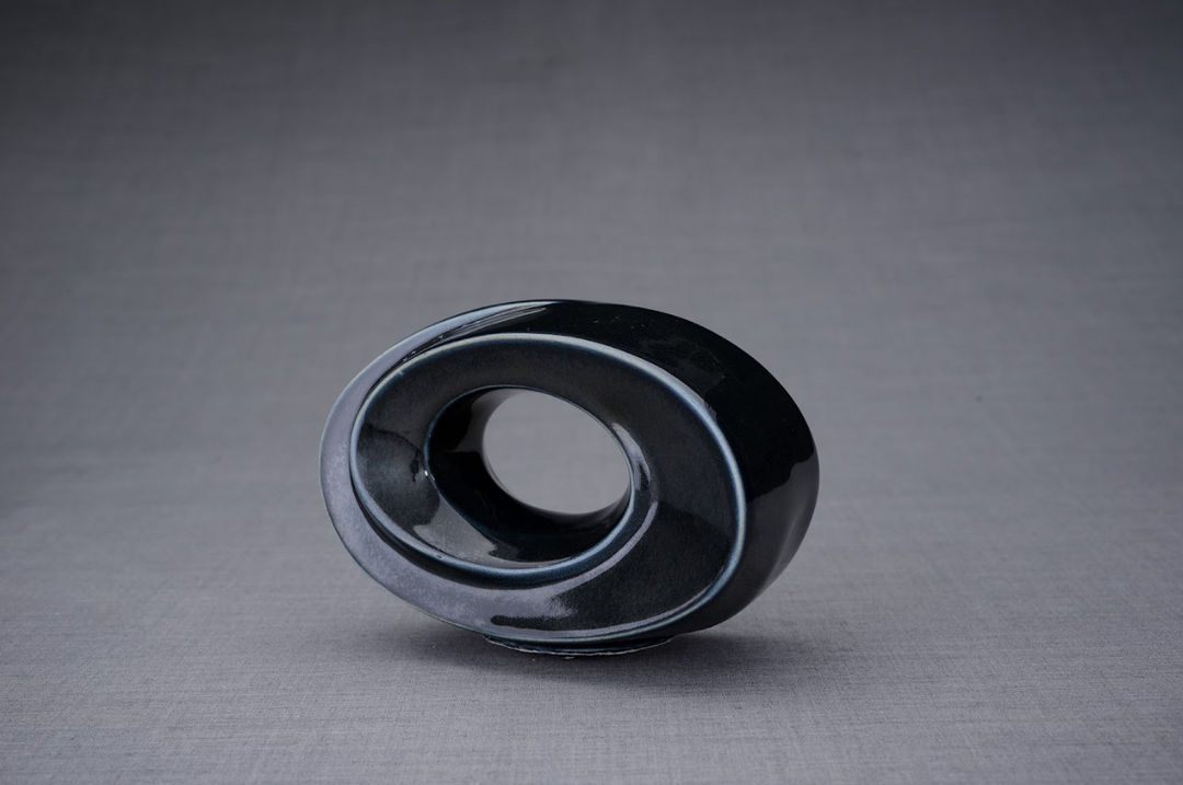 Dark glossy The Passage Ceramic Urn with a fluid spiral form and a lit candle visible in the central ring.