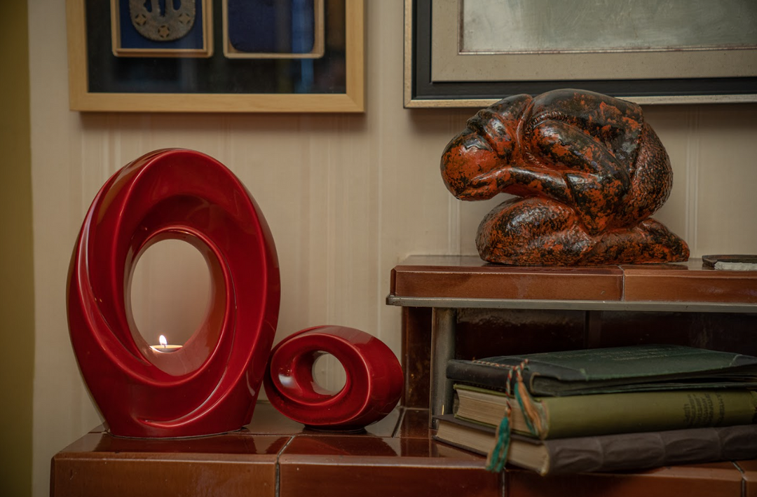 Two red glossy ceramic loop urns on a wooden surface, one with a lit candle inside the inner circle.