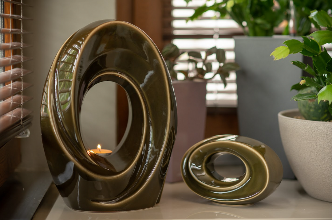 Two olive glazed ceramic sculptures with circular ring shapes, the larger one containing a candle in its inner opening.